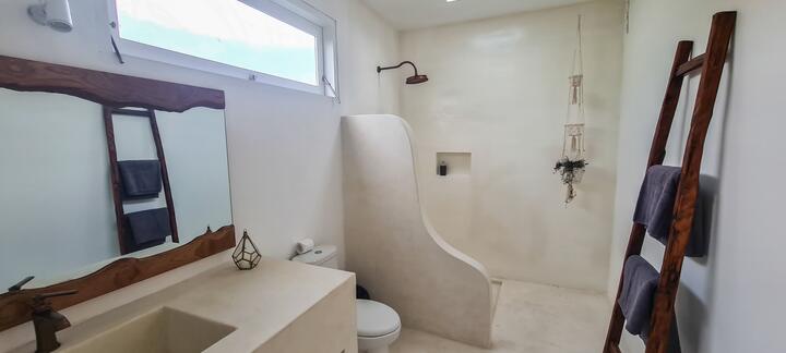 White en-suite bathroom with a curved walk-in shower, teak towel ladder and high window