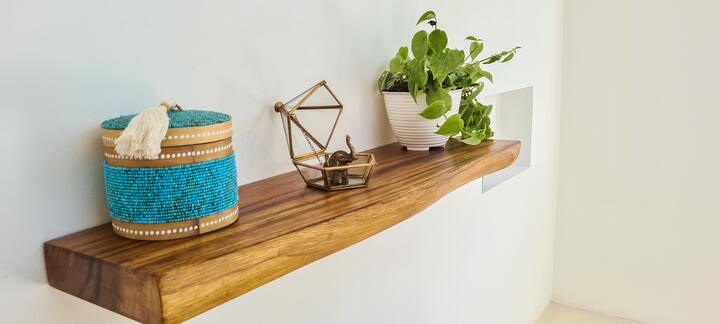 Teak floating shelf with a turquoise woven basket, a brass terrarium and a trailing plant