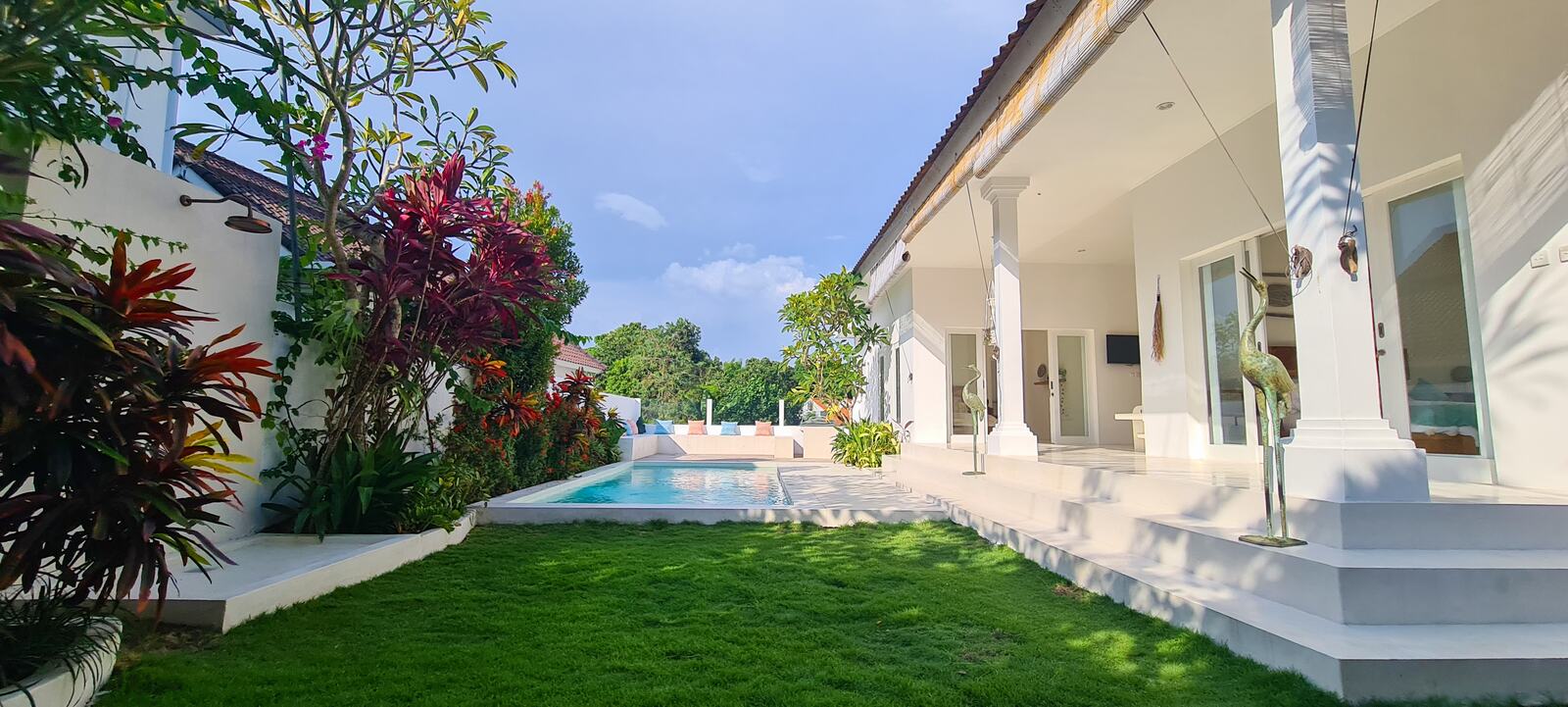Green lawn and tropical planting running beside the pool and the villa's white columned terrace