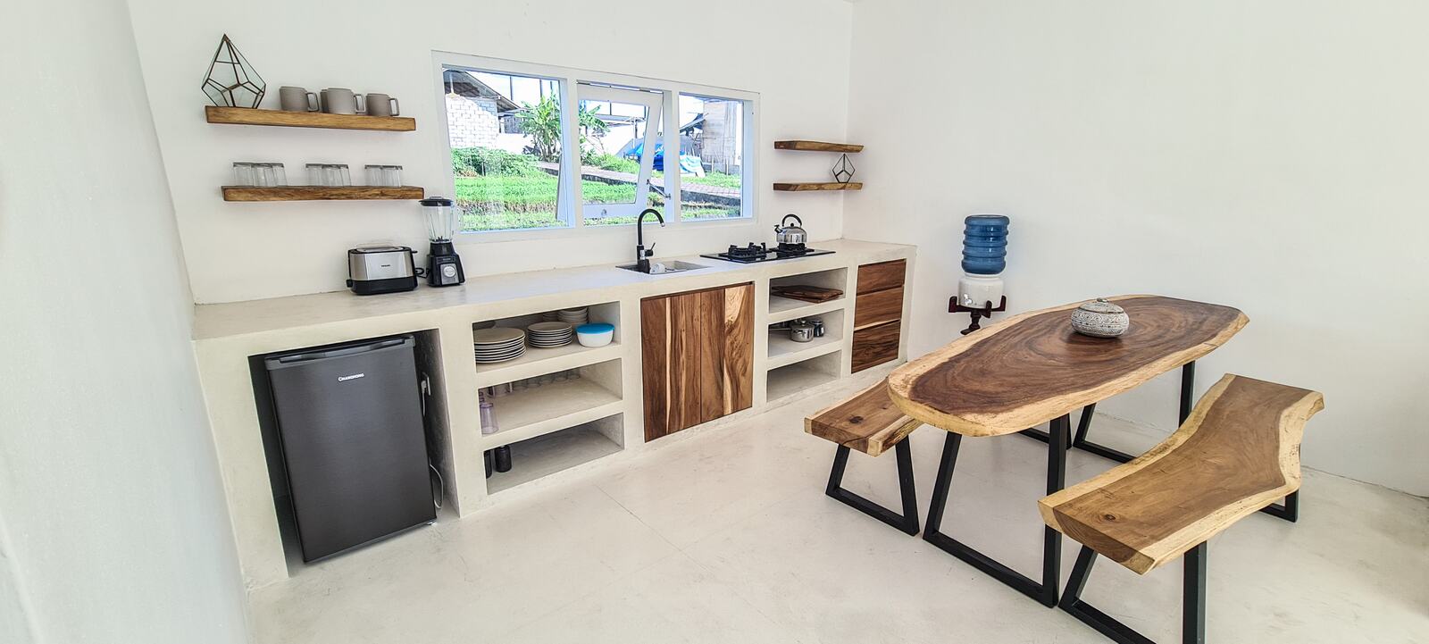 White kitchen with open shelves, gas stove, fridge, water dispenser and a live-edge teak dining table with benches