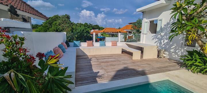 Wooden sun deck with built-in seating and colourful cushions at the end of the pool